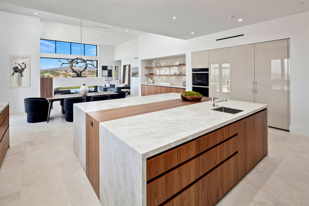 Large contemporary u-shaped open plan kitchen in San Diego with a single-bowl sink, flat-panel cabinets, beige cabinets, marble worktops, white splashback, marble splashback, stainless steel appliances, limestone flooring, an island, beige floors and white worktops.