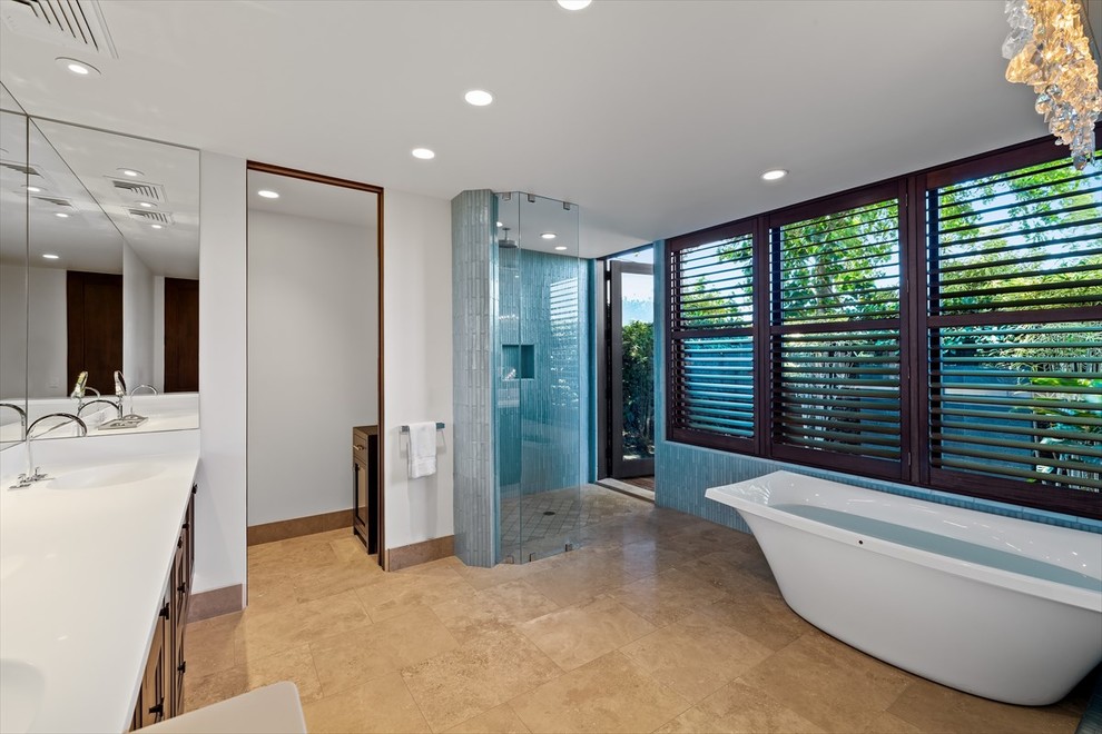 Design ideas for a large contemporary bathroom in Hawaii with recessed-panel cabinets, dark wood cabinets, a freestanding tub, a curbless shower, a wall-mount toilet, white tile, glass sheet wall, white walls, dark hardwood floors, an undermount sink, solid surface benchtops, brown floor, a hinged shower door and white benchtops.