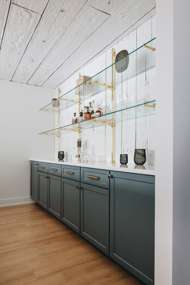 This is an example of a large eclectic single-wall seated home bar in Grand Rapids with no sink, glass-front cabinets, blue cabinets, quartz benchtops, white splashback, timber splashback, light hardwood floors and white benchtop.