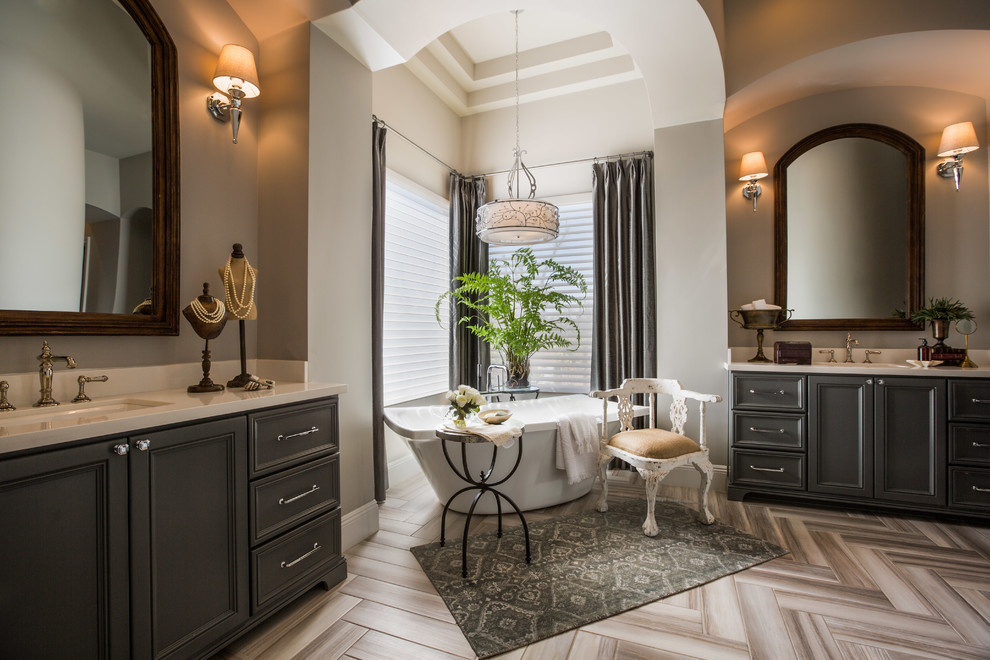 Example of a transitional master porcelain tile and gray tile porcelain tile freestanding bathtub design in Phoenix with recessed-panel cabinets, gray cabinets, a one-piece toilet, gray walls, an undermount sink and solid surface countertops