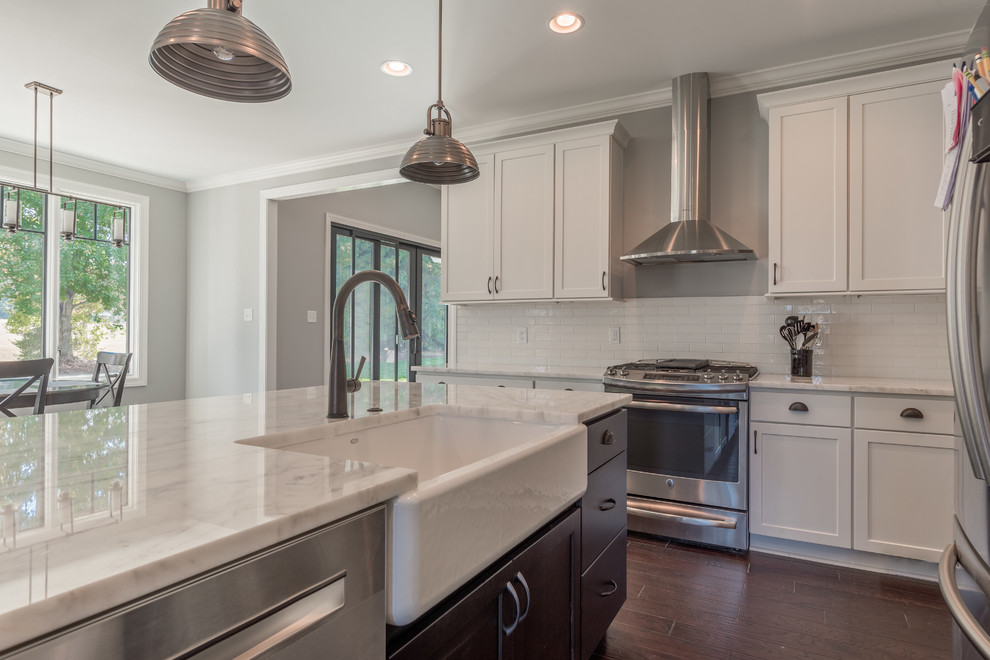 Mid-sized transitional dark wood floor eat-in kitchen photo with a farmhouse sink, shaker cabinets, white cabinets, marble countertops, white backsplash, subway tile backsplash, stainless steel appliances and an island