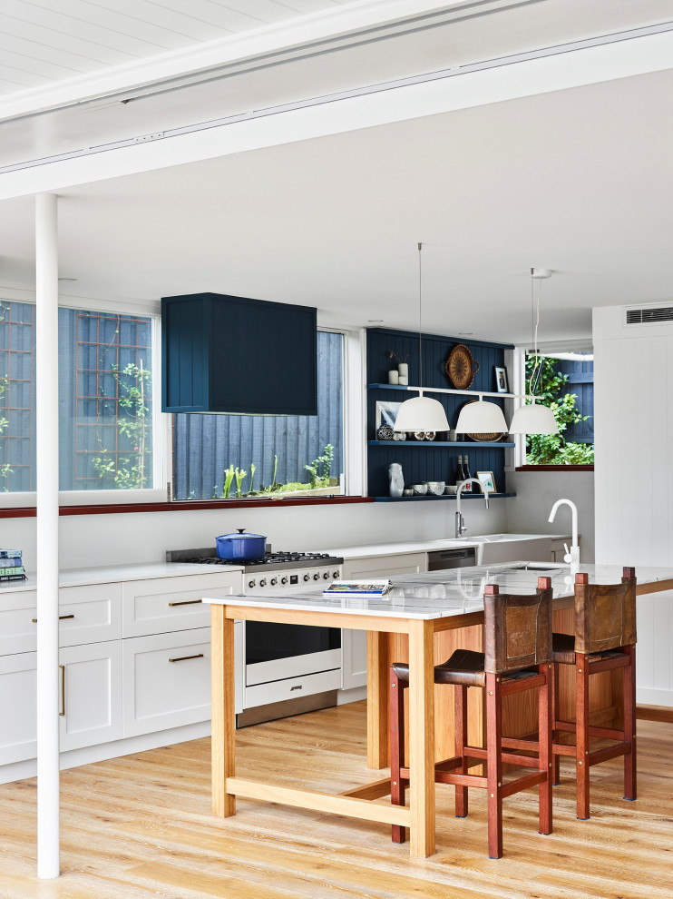 Inspiration for a medium sized contemporary galley open plan kitchen in Brisbane with a belfast sink, shaker cabinets, white cabinets, marble worktops, white splashback, window splashback, stainless steel appliances, light hardwood flooring, an island, brown floors, white worktops and a drop ceiling.