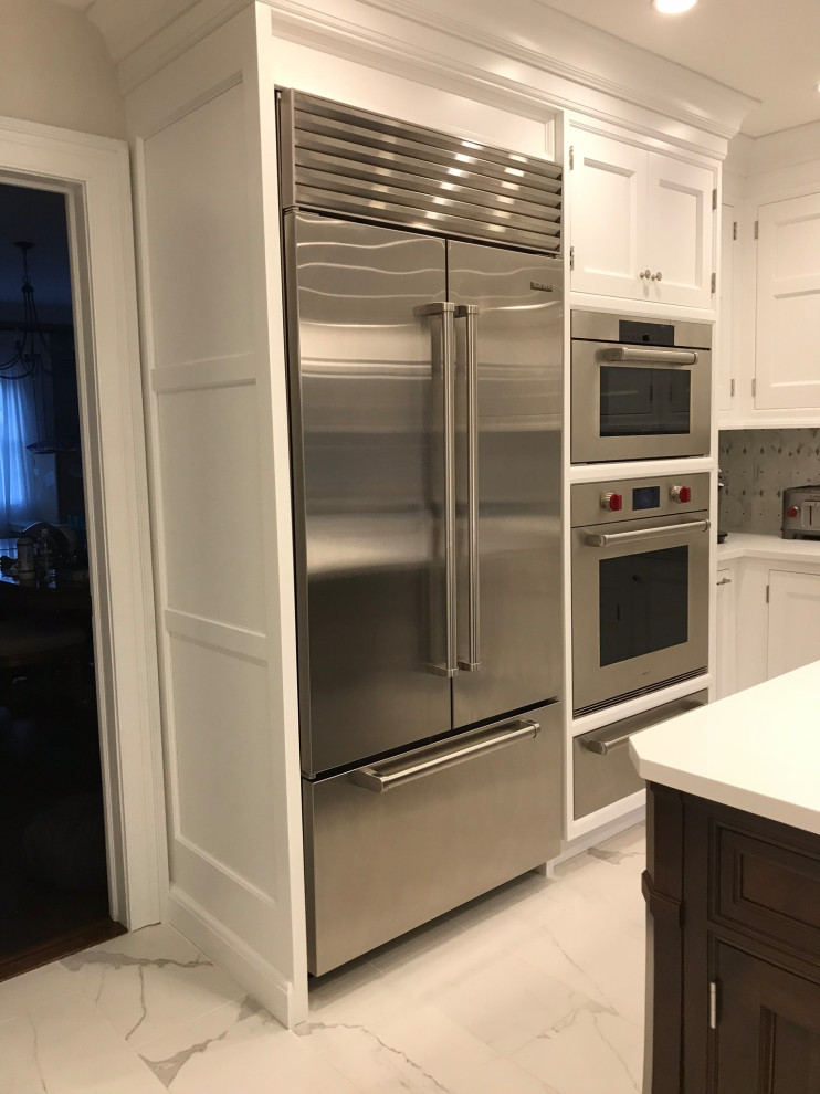 Mid-sized transitional l-shaped eat-in kitchen in New York with an undermount sink, recessed-panel cabinets, white cabinets, quartz benchtops, white splashback, marble splashback, stainless steel appliances, marble floors, with island, white floor and white benchtop.