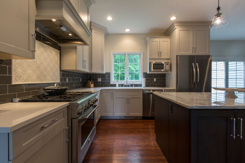 Design ideas for a mid-sized transitional l-shaped eat-in kitchen in Bridgeport with an undermount sink, recessed-panel cabinets, grey cabinets, granite benchtops, black splashback, ceramic splashback, stainless steel appliances, medium hardwood floors and with island.