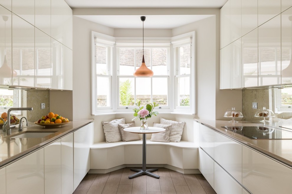 Design ideas for a mid-sized contemporary galley eat-in kitchen in London with flat-panel cabinets, white cabinets, mirror splashback, brown floor, beige benchtop, an undermount sink, metallic splashback, panelled appliances, dark hardwood floors and no island.