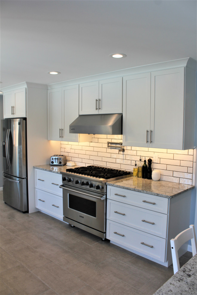 This is an example of a large galley eat-in kitchen in Detroit with an undermount sink, shaker cabinets, white cabinets, granite benchtops, white splashback, ceramic splashback, stainless steel appliances, terra-cotta floors, with island, grey floor and white benchtop.