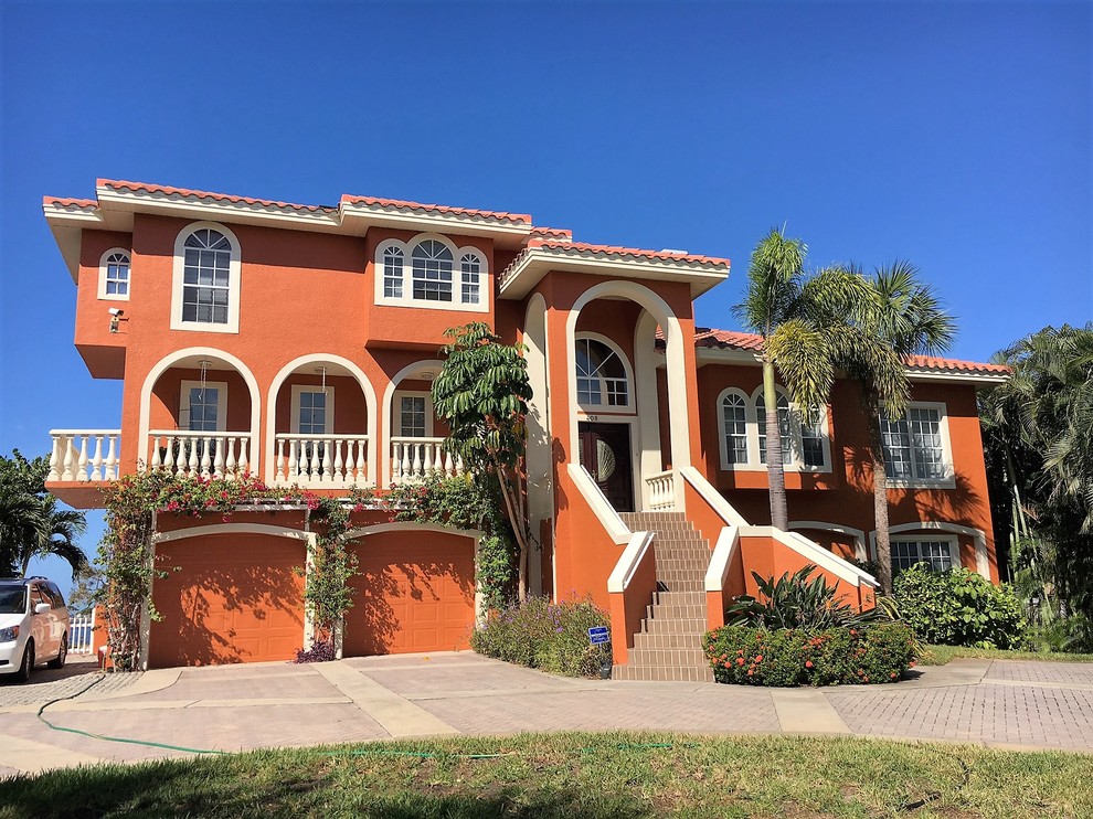 This is an example of a large tropical two-storey stucco red house exterior in Tampa with a hip roof and a tile roof.