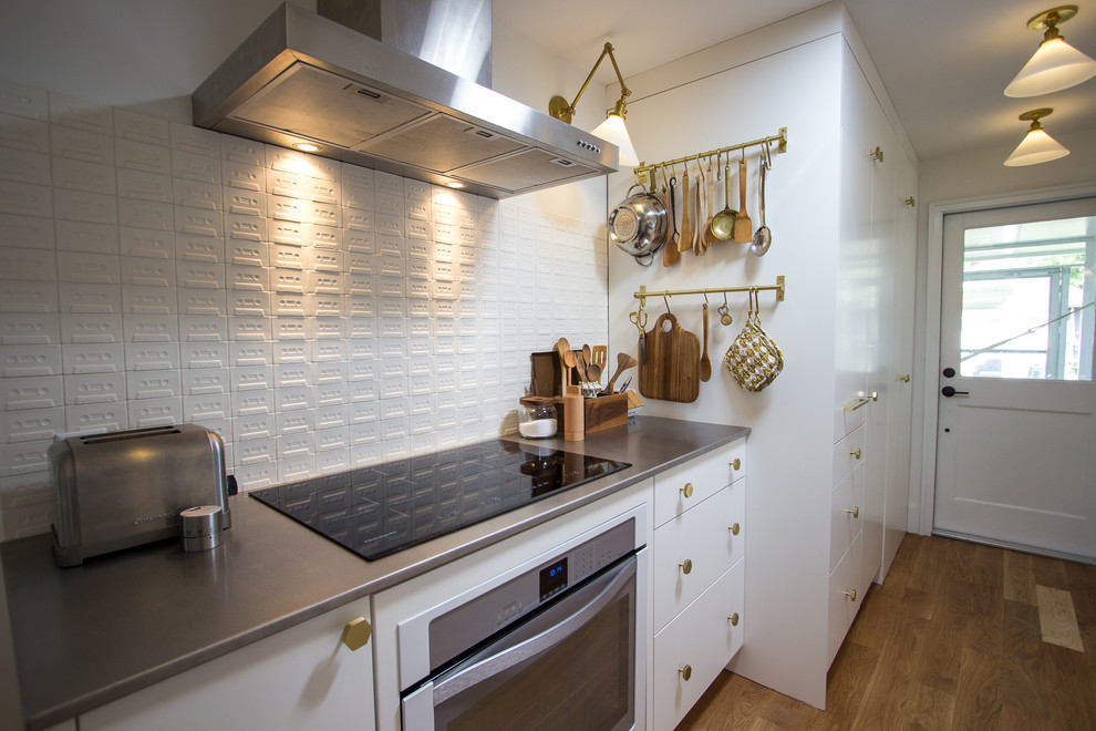 Small traditional galley separate kitchen in Houston with an integrated sink, flat-panel cabinets, white cabinets, stainless steel benchtops, white splashback, ceramic splashback, stainless steel appliances, light hardwood floors, no island and brown floor.