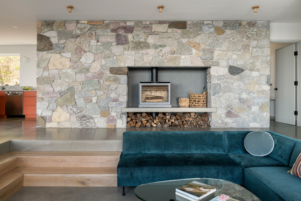 Aménagement d'un salon contemporain de taille moyenne et ouvert avec un mur gris, sol en béton ciré, un poêle à bois, un manteau de cheminée en pierre, un téléviseur encastré et un sol gris.
