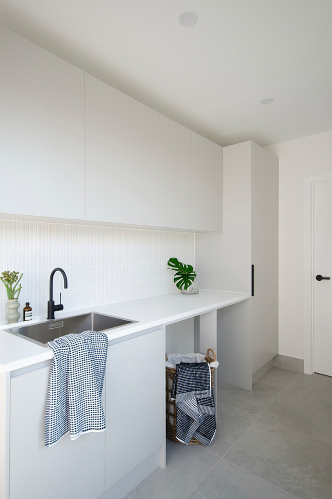 Design ideas for a mid-sized modern single-wall dedicated laundry room in Canberra - Queanbeyan with a single-bowl sink, laminate benchtops, white splashback, mosaic tile splashback, white walls, porcelain floors, a side-by-side washer and dryer, grey floor and white benchtop.