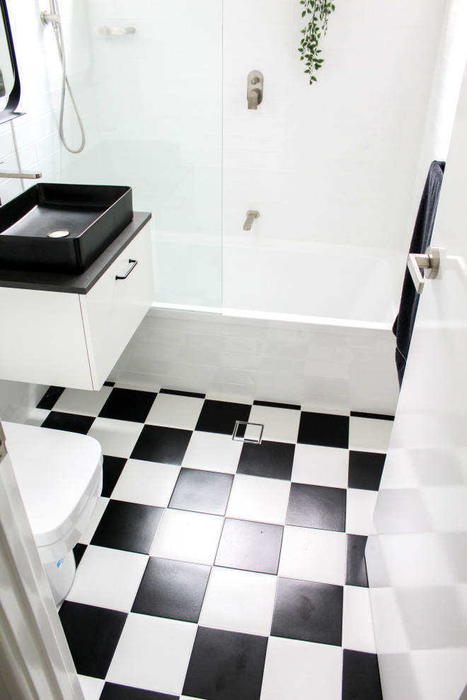 Design ideas for a small modern 3/4 bathroom in Perth with flat-panel cabinets, white cabinets, an alcove tub, a shower/bathtub combo, a one-piece toilet, white tile, ceramic tile, white walls, porcelain floors, a vessel sink, engineered quartz benchtops, multi-coloured floor, black benchtops, a single vanity and a floating vanity.
