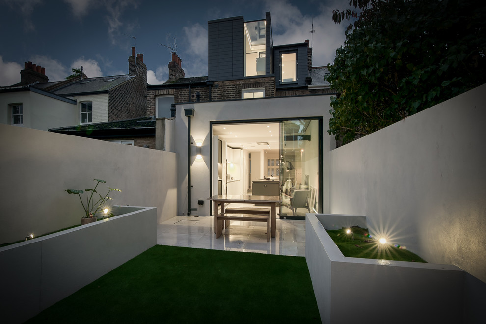 Photo of a small contemporary three-storey stucco white townhouse exterior in London with a flat roof and a tile roof.
