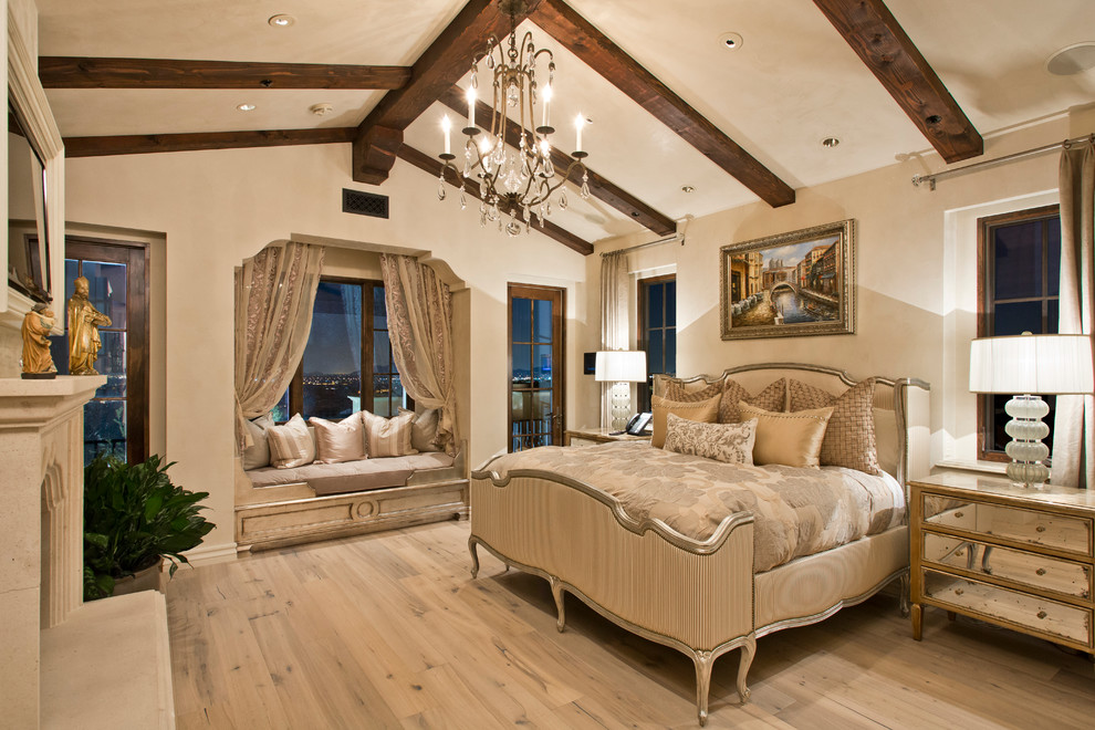 Photo of a large mediterranean master bedroom in Phoenix with beige walls, vinyl floors, a standard fireplace, a stone fireplace surround and beige floor.