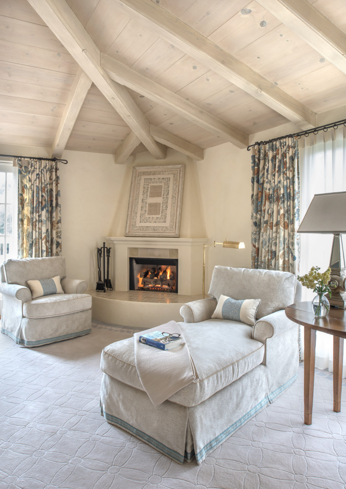 This is an example of a large traditional master bedroom in Santa Barbara with beige walls, carpet, a corner fireplace, a plaster fireplace surround, beige floor and exposed beam.