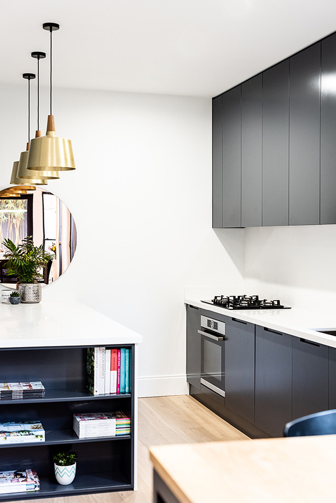 Design ideas for a small contemporary galley open plan kitchen in Sydney with an undermount sink, flat-panel cabinets, black cabinets, quartz benchtops, white splashback, stone slab splashback, stainless steel appliances, light hardwood floors, with island, brown floor and white benchtop.