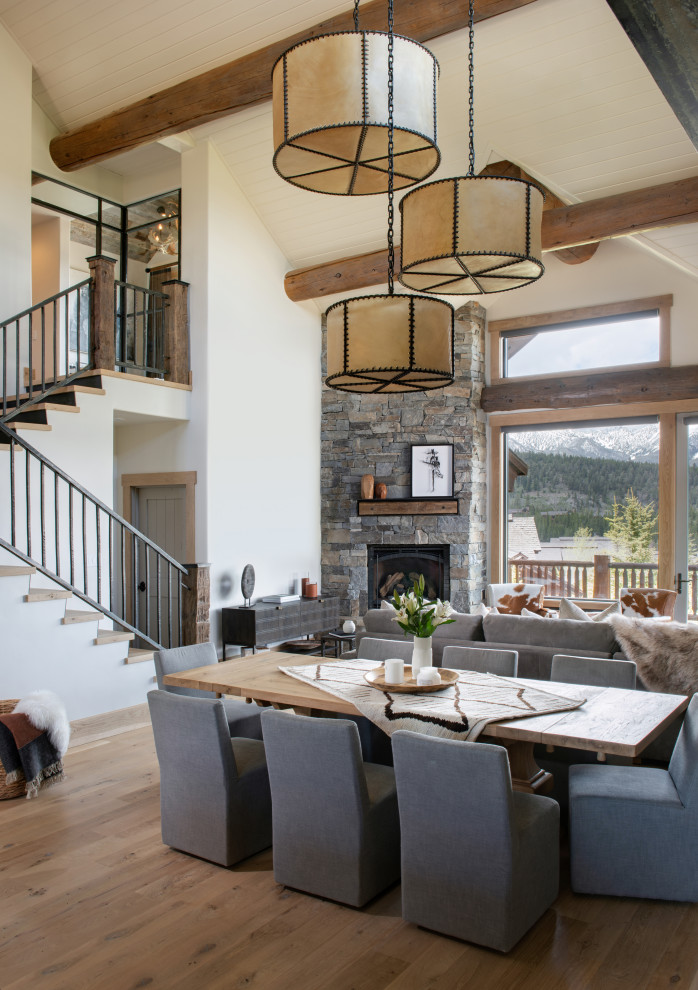 This is an example of a mid-sized country open plan dining in Other with white walls, medium hardwood floors, a corner fireplace, a stone fireplace surround, brown floor and vaulted.