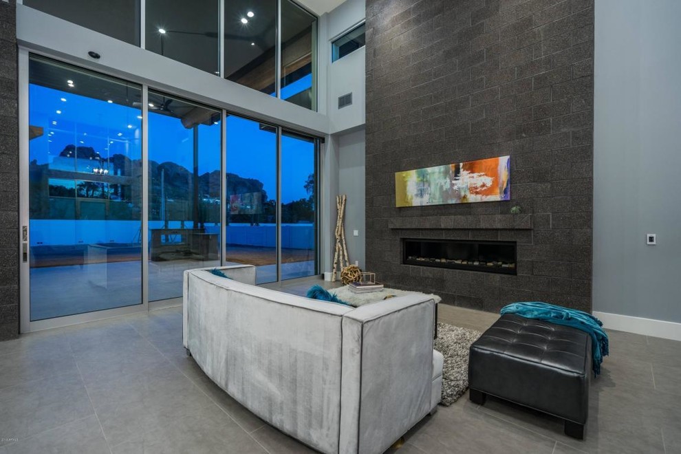 Photo of an expansive modern open concept family room in Phoenix with a home bar, white walls, porcelain floors, a standard fireplace, a stone fireplace surround, a wall-mounted tv and grey floor.