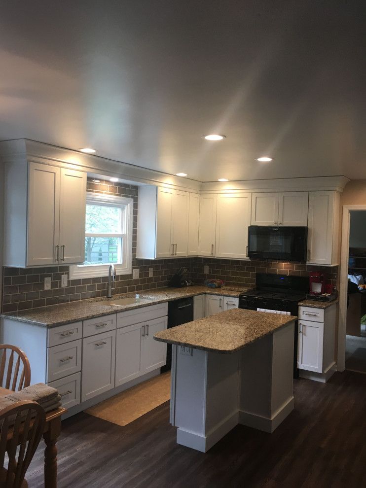 Mid-sized transitional u-shaped dark wood floor and gray floor eat-in kitchen photo with an undermount sink, shaker cabinets, white cabinets, granite countertops, gray backsplash, ceramic backsplash, black appliances, an island and beige countertops