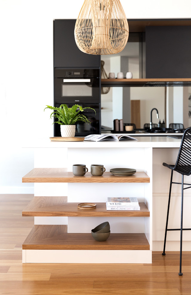 Inspiration for a large contemporary galley eat-in kitchen in Gold Coast - Tweed with a drop-in sink, flat-panel cabinets, light wood cabinets, quartz benchtops, mirror splashback, black appliances, light hardwood floors, with island and brown floor.