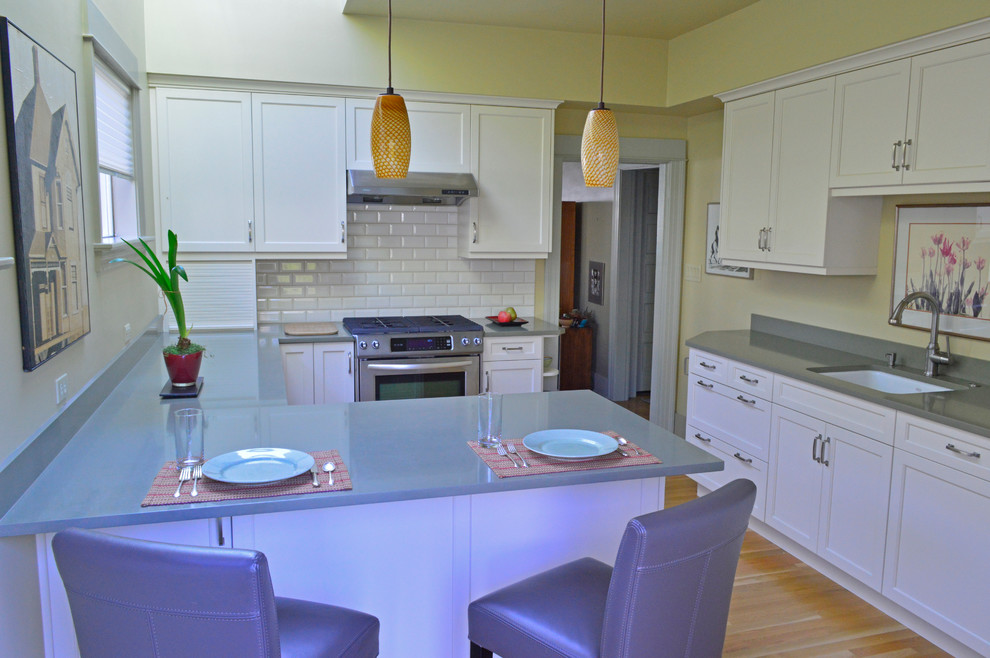 Inspiration for a mid-sized transitional light wood floor enclosed kitchen remodel in Seattle with an undermount sink, recessed-panel cabinets, white cabinets, quartz countertops, white backsplash, subway tile backsplash, stainless steel appliances and a peninsula