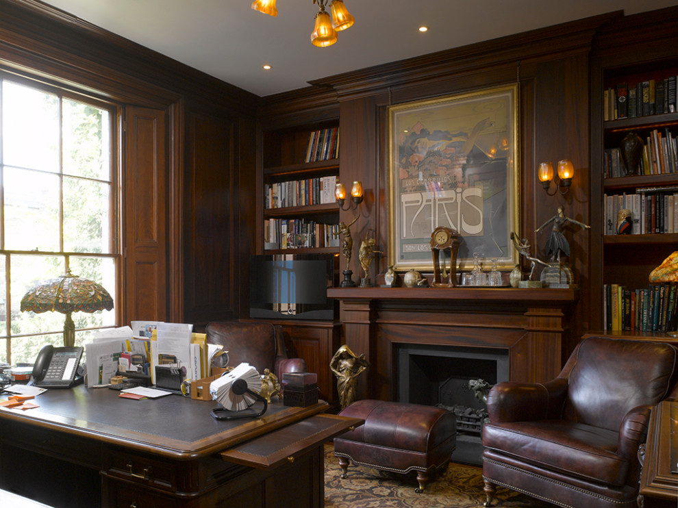 Inspiration for a mid-sized traditional study room in London with brown walls, dark hardwood floors, a standard fireplace, a freestanding desk, brown floor and wood walls.