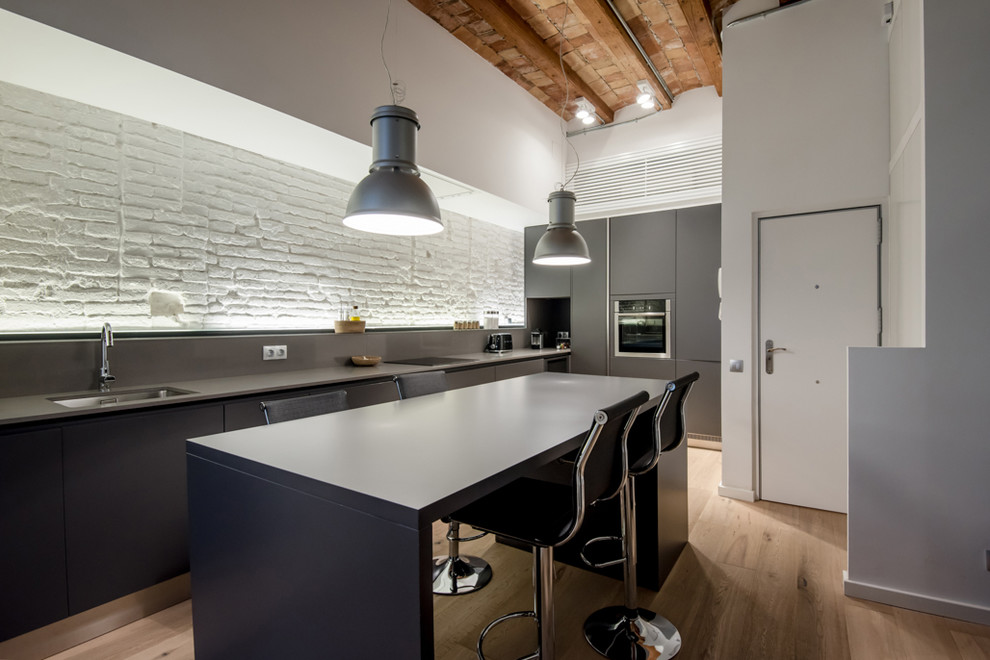 Mid-sized industrial single-wall open plan kitchen in Barcelona with an undermount sink, flat-panel cabinets, grey cabinets, medium hardwood floors, with island and brown floor.