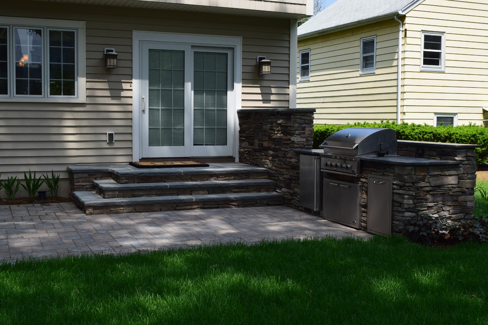 This is an example of a mid-sized country backyard patio in New York with an outdoor kitchen, concrete pavers and no cover.
