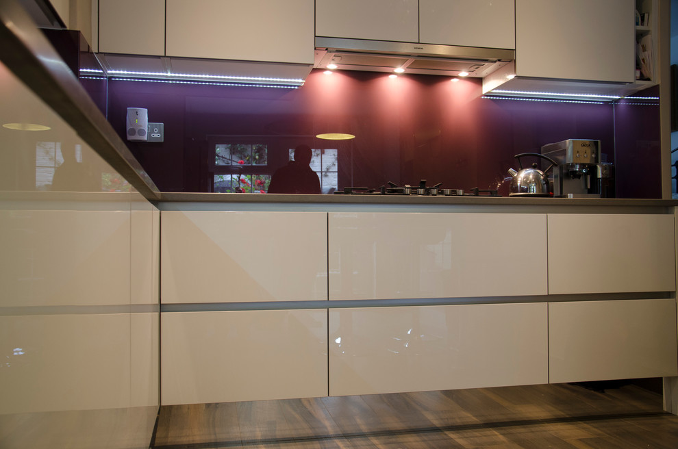 This is an example of a large modern eat-in kitchen in London with a double-bowl sink, flat-panel cabinets, white cabinets, solid surface benchtops, glass sheet splashback, stainless steel appliances, porcelain floors and a peninsula.
