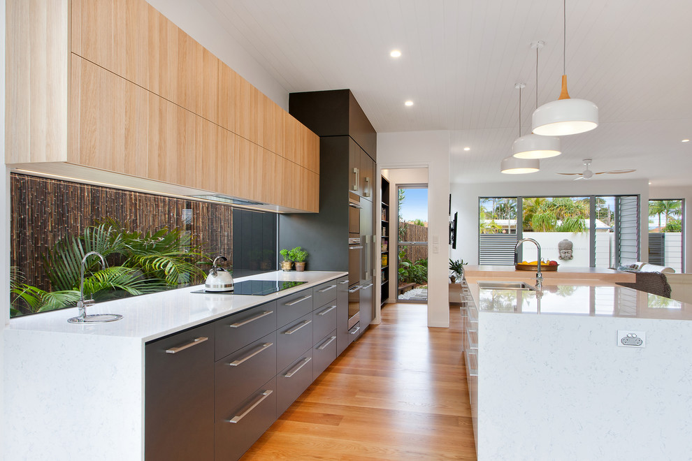 Inspiration for a large beach style galley open plan kitchen in Sunshine Coast with flat-panel cabinets, medium hardwood floors, multiple islands, brown floor, white benchtop, an undermount sink, window splashback and panelled appliances.