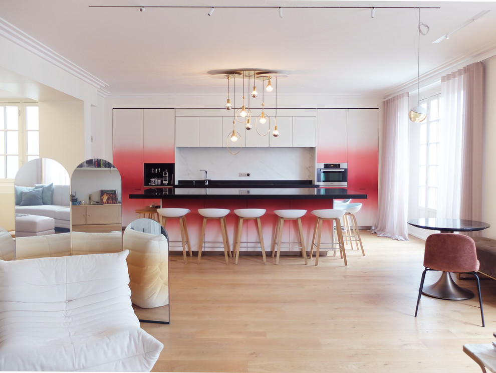 This is an example of a large contemporary single-wall open plan kitchen in Paris with an undermount sink, red cabinets, granite benchtops, white splashback, marble splashback, stainless steel appliances, light hardwood floors, with island, black benchtop, flat-panel cabinets and beige floor.