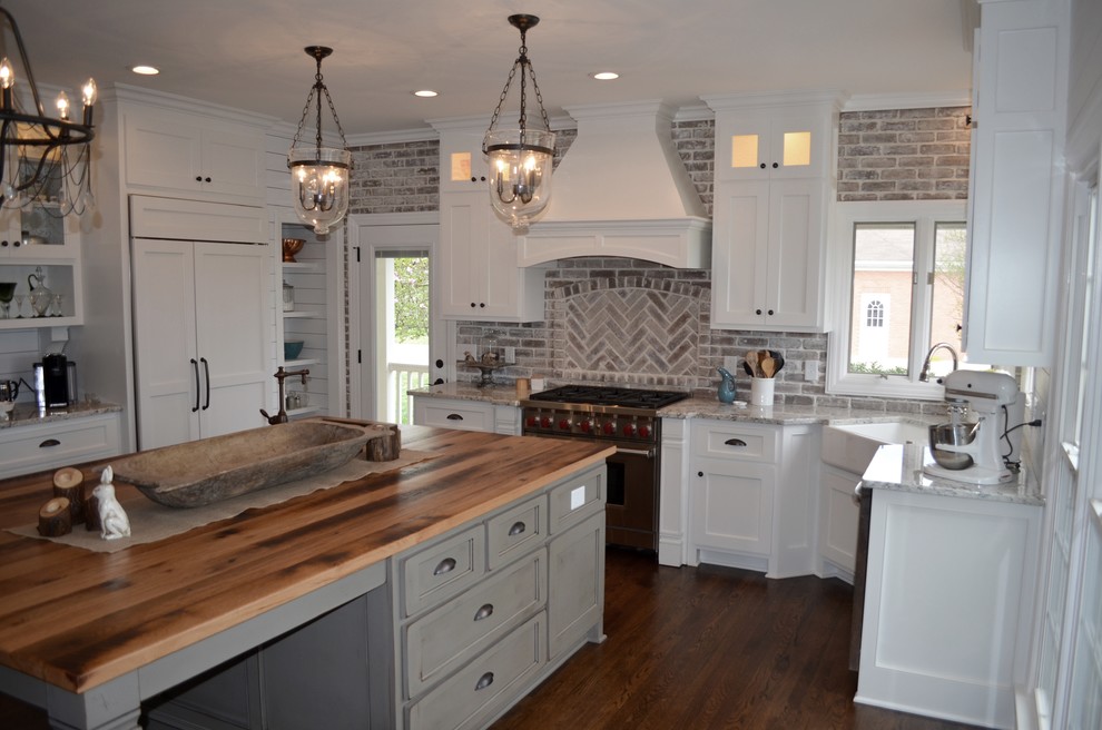 Design ideas for a mid-sized country u-shaped separate kitchen in Nashville with a farmhouse sink, shaker cabinets, white cabinets, granite benchtops, beige splashback, brick splashback, panelled appliances, medium hardwood floors, with island and brown floor.