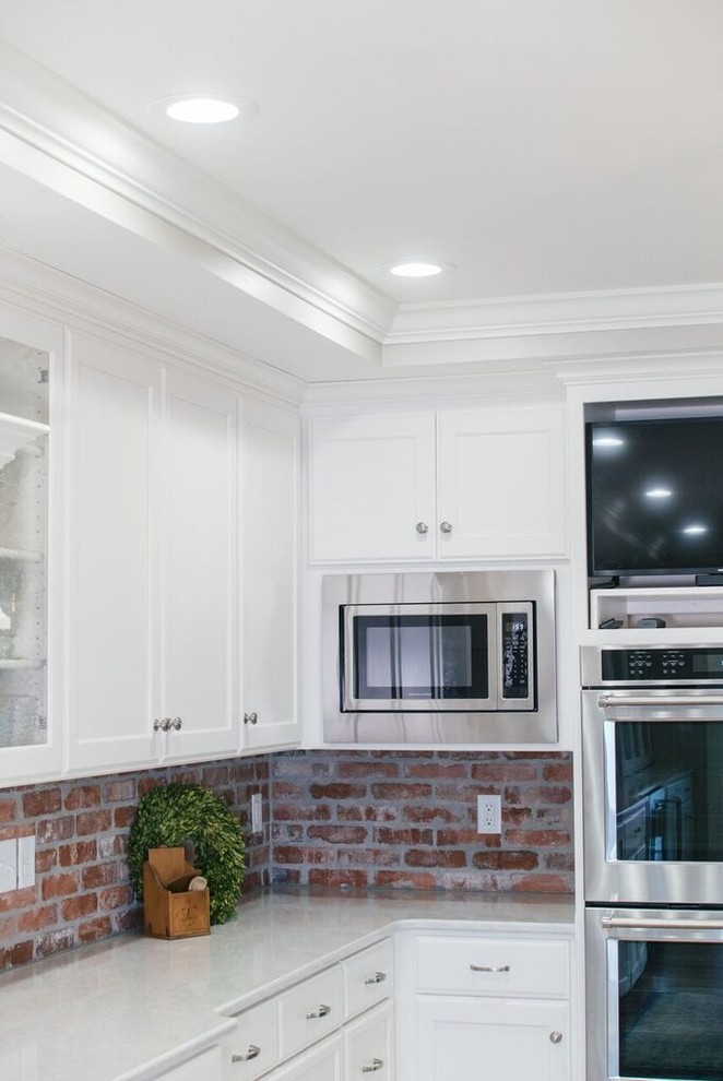 Huge l-shaped light wood floor and brown floor open concept kitchen photo with a double-bowl sink, recessed-panel cabinets, brick backsplash, stainless steel appliances and an island