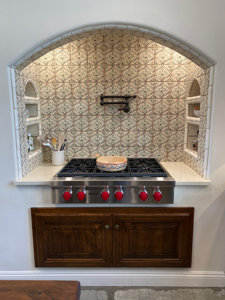 Inspiration for a mid-sized rustic u-shaped concrete floor and gray floor eat-in kitchen remodel in Phoenix with a farmhouse sink, raised-panel cabinets, distressed cabinets, wood countertops, multicolored backsplash, ceramic backsplash, stainless steel appliances, an island and brown countertops