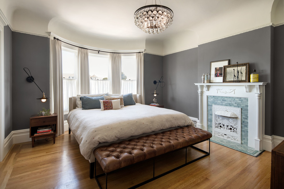 Photo of a mid-sized transitional master bedroom in San Francisco with grey walls, a standard fireplace, a tile fireplace surround, brown floor and light hardwood floors.