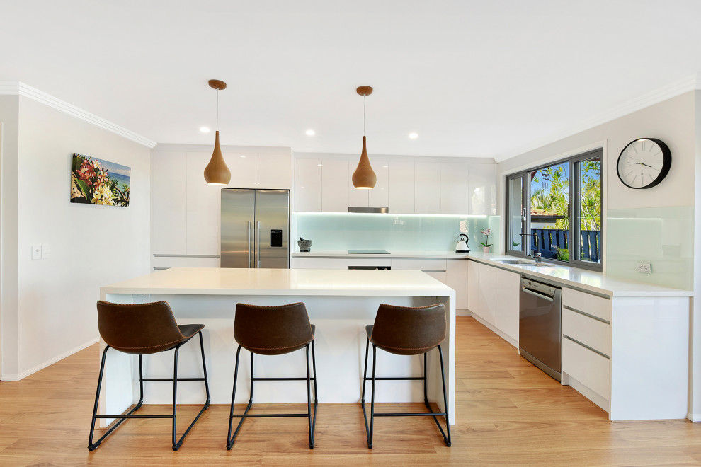 Design ideas for a contemporary l-shaped kitchen in Gold Coast - Tweed with a double-bowl sink, flat-panel cabinets, white cabinets, glass sheet splashback, stainless steel appliances, dark hardwood floors, with island, beige floor and white benchtop.