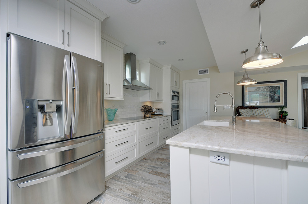 Inspiration for a mid-sized beach style single-wall open plan kitchen in Tampa with a farmhouse sink, shaker cabinets, white cabinets, granite benchtops, white splashback, ceramic splashback, stainless steel appliances, vinyl floors and with island.
