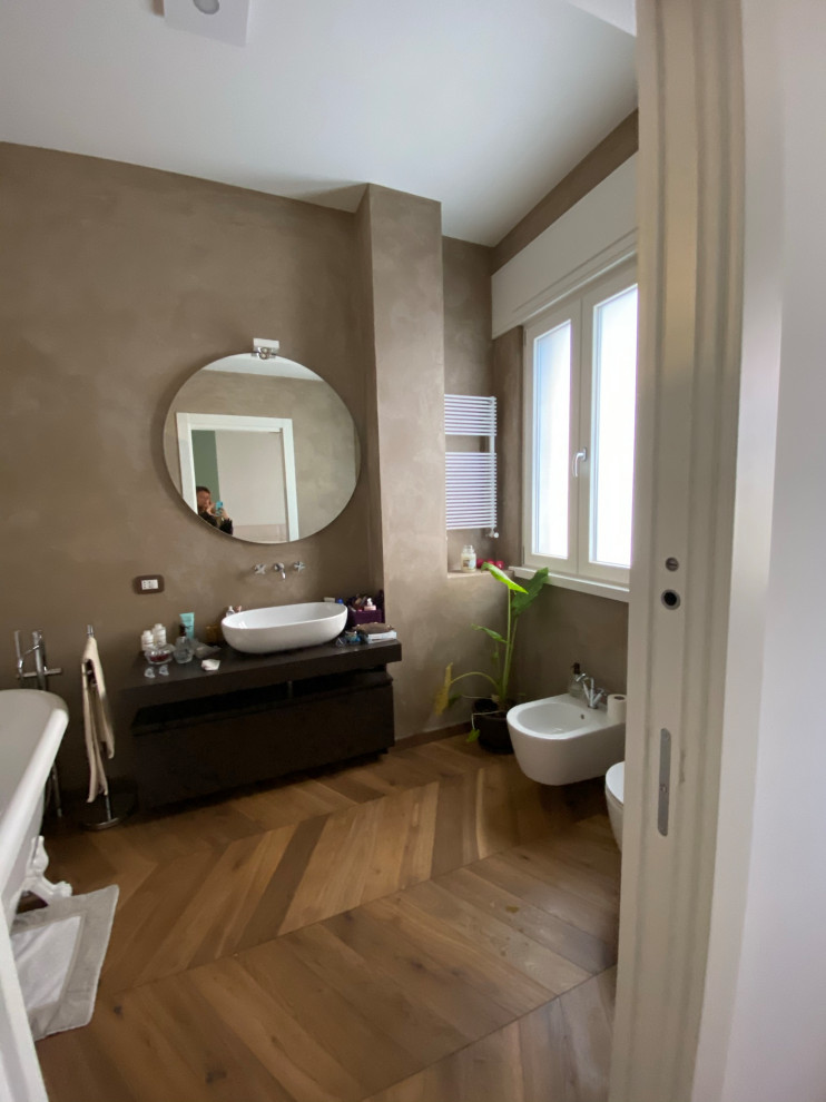 Photo of a mid-sized modern master bathroom in Other with furniture-like cabinets, brown cabinets, a claw-foot tub, a wall-mount toilet, beige walls, dark hardwood floors, a vessel sink, wood benchtops, brown floor, brown benchtops, a single vanity, a freestanding vanity and recessed.