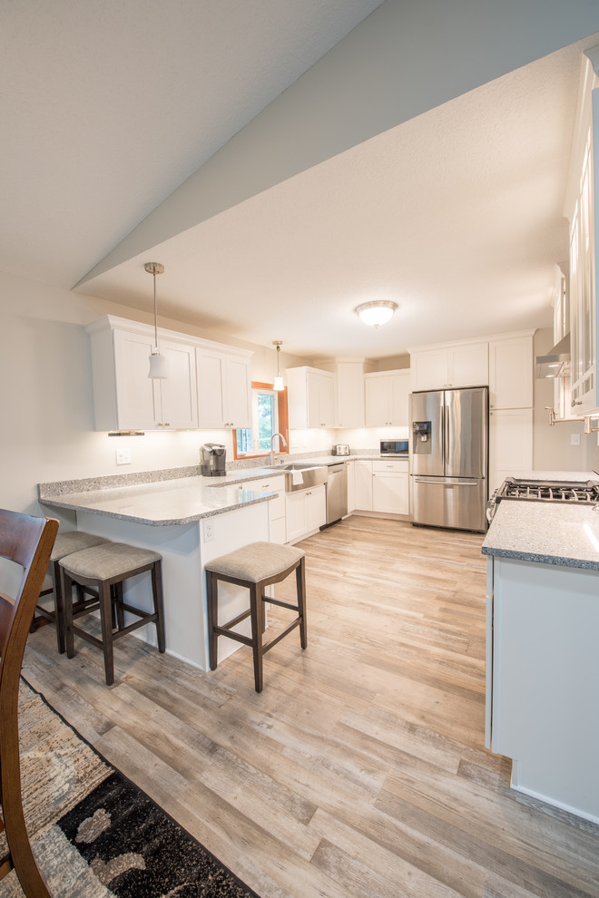Inspiration for a large transitional u-shaped light wood floor and brown floor enclosed kitchen remodel in Minneapolis with a farmhouse sink, shaker cabinets, white cabinets, granite countertops, stainless steel appliances, a peninsula and gray countertops
