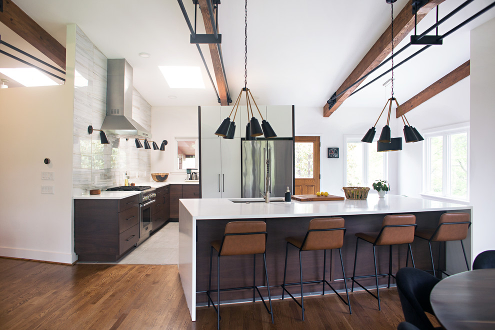 This is an example of a midcentury u-shaped kitchen in Cincinnati with an undermount sink, flat-panel cabinets, dark wood cabinets, white splashback, stainless steel appliances, dark hardwood floors, with island, brown floor and white benchtop.
