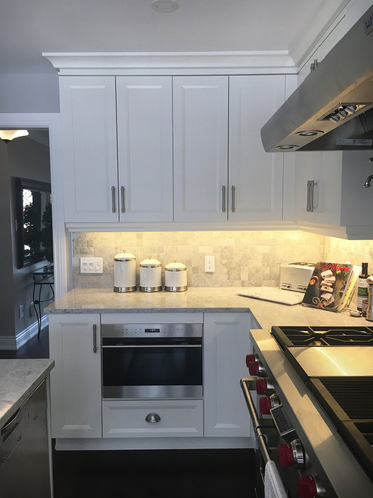 Transitional l-shaped brown floor eat-in kitchen photo with a farmhouse sink, white cabinets, quartz countertops, stainless steel appliances, an island and white countertops