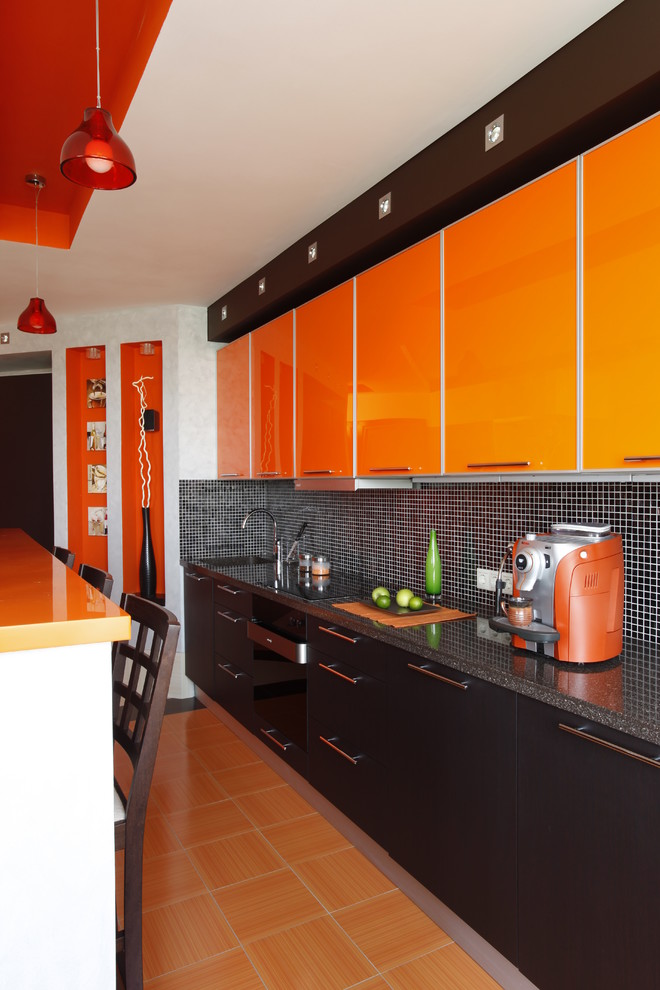 This is an example of a contemporary single-wall open plan kitchen in Moscow with an integrated sink, orange cabinets, solid surface benchtops, mosaic tile splashback, black appliances, ceramic floors, flat-panel cabinets, black splashback and with island.
