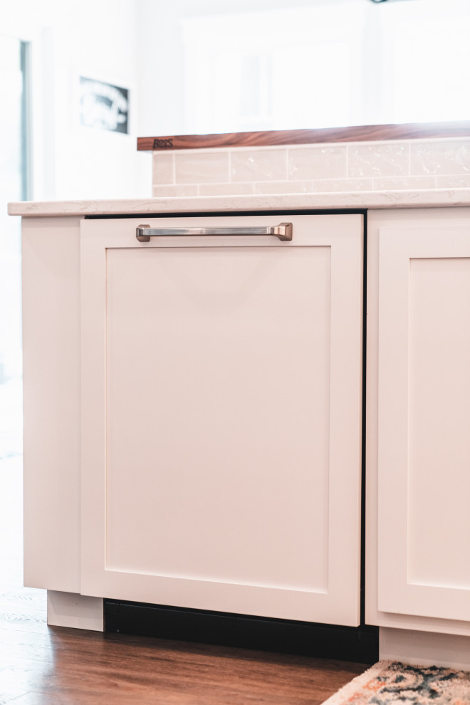 Large transitional l-shaped vinyl floor and brown floor kitchen pantry photo with an undermount sink, shaker cabinets, white cabinets, quartz countertops, gray backsplash, subway tile backsplash, stainless steel appliances, an island and white countertops