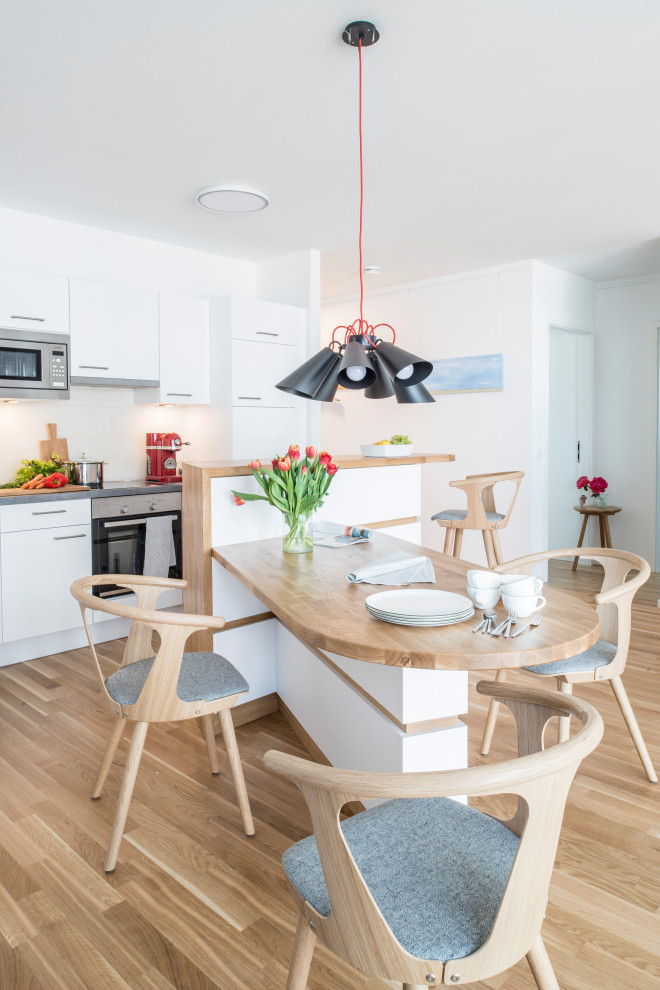 This is an example of a contemporary galley eat-in kitchen in Hamburg with with island, flat-panel cabinets, white cabinets, light hardwood floors, beige floor and grey benchtop.