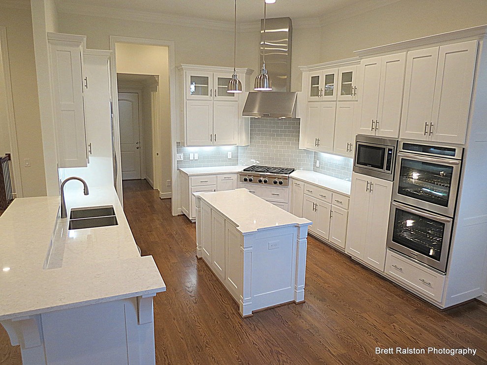 Example of a mid-sized transitional medium tone wood floor eat-in kitchen design with an undermount sink, recessed-panel cabinets, quartz countertops, gray backsplash, ceramic backsplash, stainless steel appliances and an island