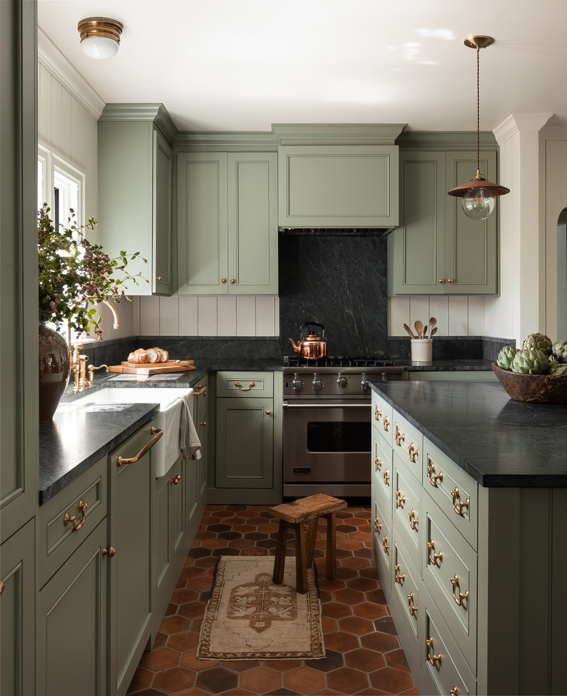 This is an example of a traditional l-shaped kitchen in Seattle with a farmhouse sink, recessed-panel cabinets, green cabinets, black splashback, with island, red floor and black benchtop.