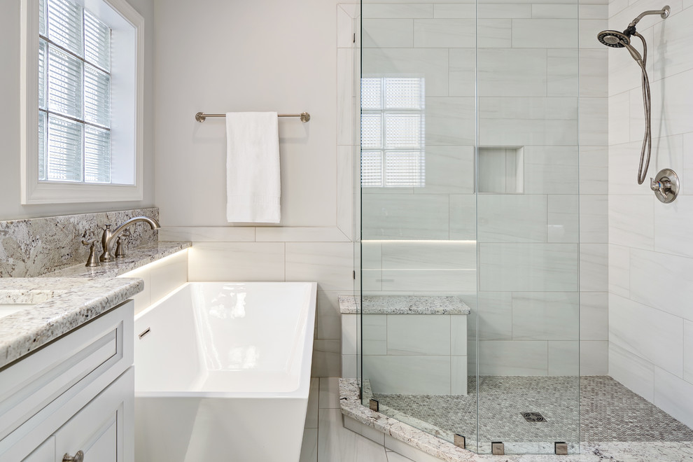 Example of a large transitional master gray tile and porcelain tile porcelain tile and gray floor freestanding bathtub design with raised-panel cabinets, white cabinets, a two-piece toilet, gray walls, an undermount sink, granite countertops and a hinged shower door