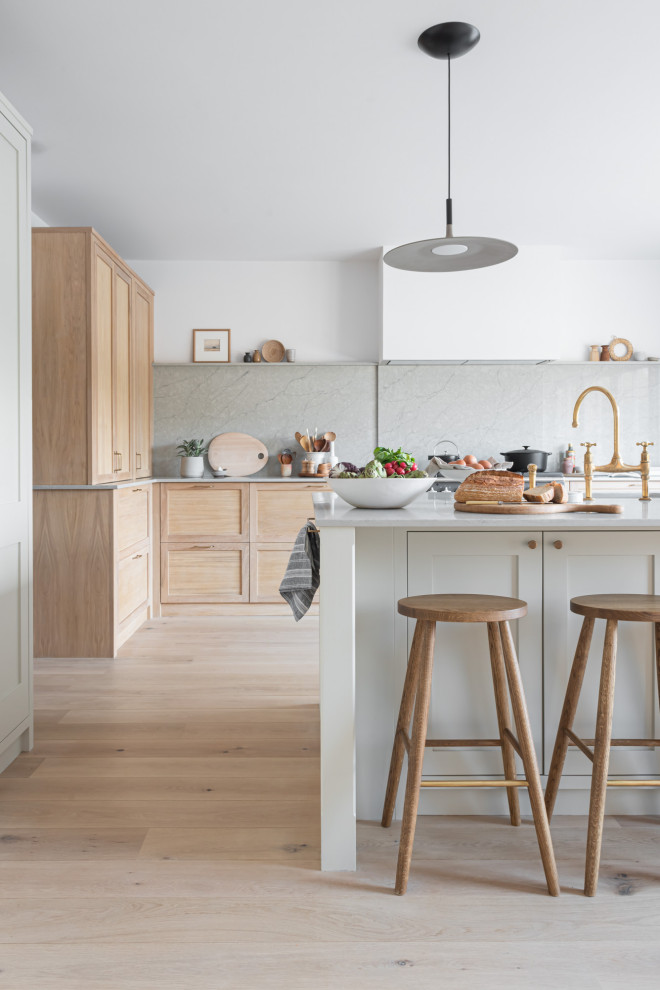 This is an example of a large scandinavian grey and cream kitchen/diner in Surrey with an integrated sink, shaker cabinets, light wood cabinets, quartz worktops, grey splashback, black appliances, light hardwood flooring, an island and grey worktops.