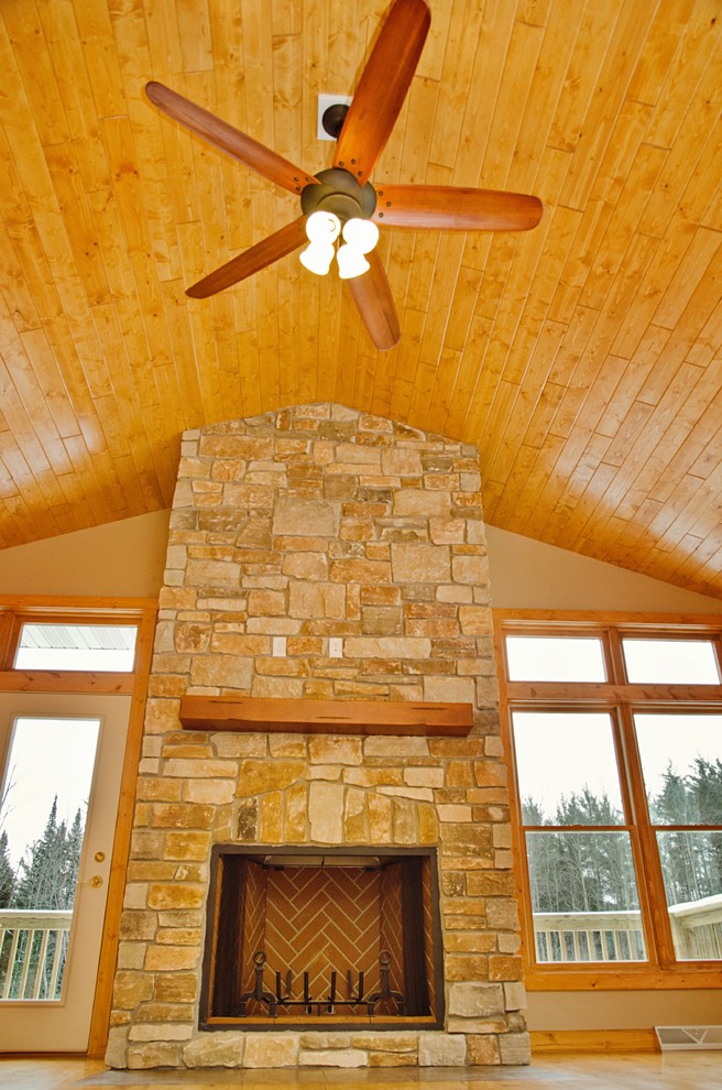 Large mountain style open concept light wood floor and brown floor home design photo with beige walls, a wood stove and a stone fireplace