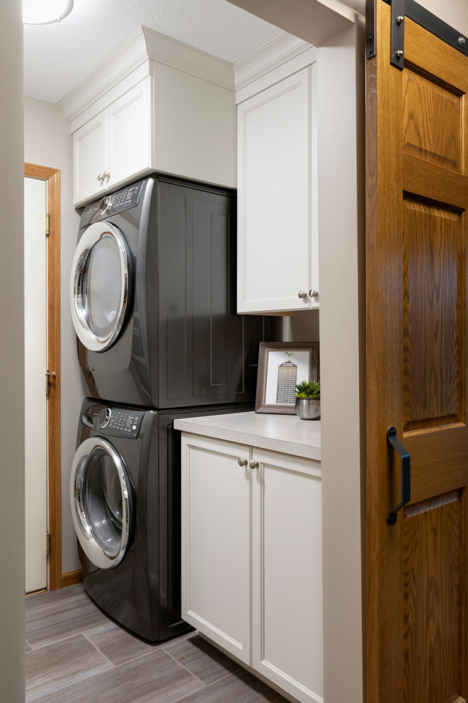 This is an example of a small transitional galley utility room in Minneapolis with flat-panel cabinets, white cabinets, laminate benchtops, white splashback, ceramic splashback, grey walls, vinyl floors, a stacked washer and dryer, grey benchtop and grey floor.