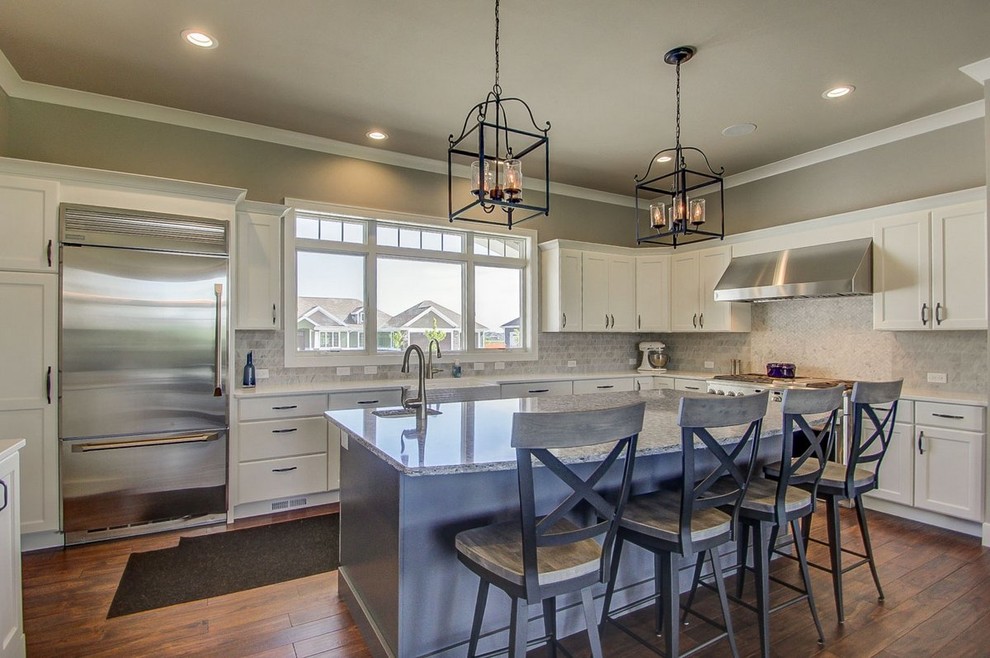 Large transitional l-shaped medium tone wood floor and brown floor kitchen photo with a farmhouse sink, recessed-panel cabinets, white cabinets, stone tile backsplash, stainless steel appliances, an island and granite countertops